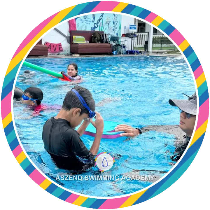 Coach helping a boy with his goggles and kickboard during a swimming lesson